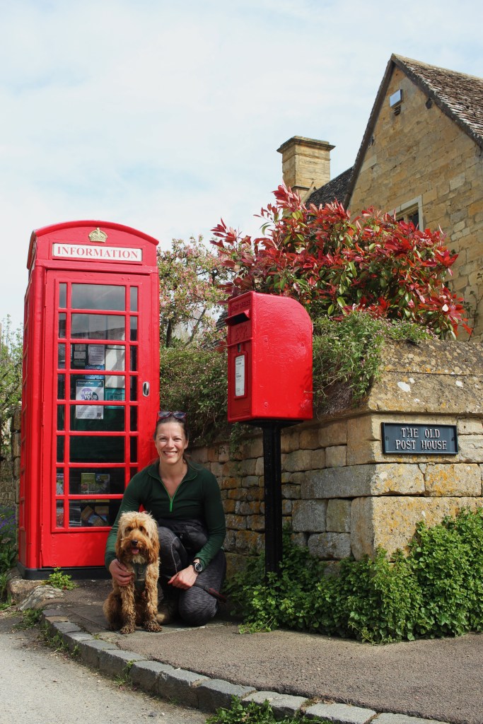 Jenn (the author) and her cockapoo Finch, sitting in front of a quintessential red UK phone booth & post box, in the village of Stanton.